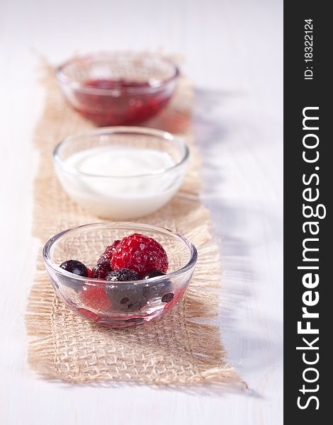 Bowls with fresh berries, jam and cream, served on white table