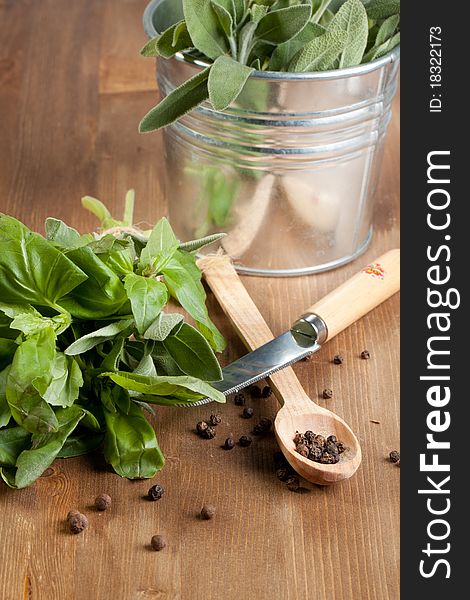 Fresh herbs with pepper, knife and spoon on wooden table