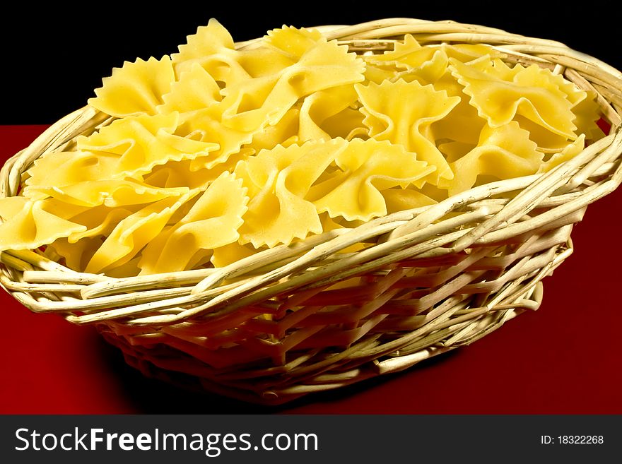 A wicker basket filled with uncooked butterfly pasta. A wicker basket filled with uncooked butterfly pasta