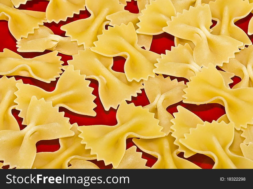 A close up of bow-tie pasta on a red background. A close up of bow-tie pasta on a red background