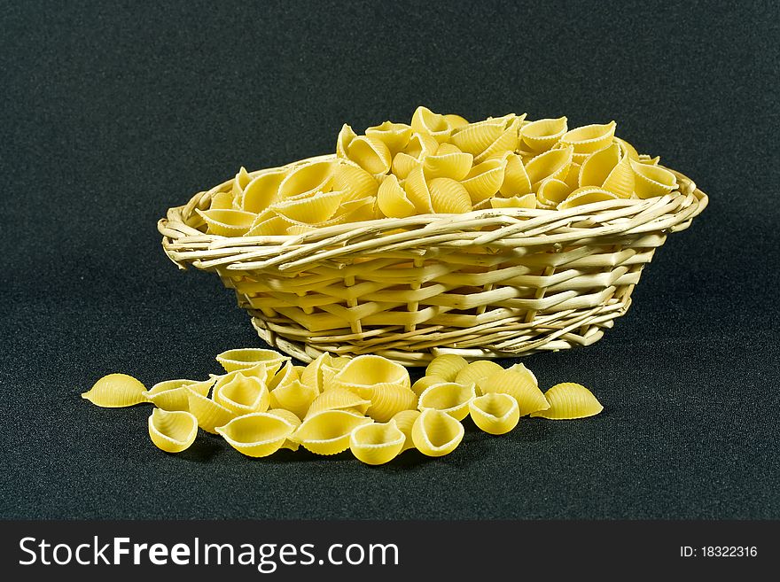 A closeup of a wicker basket containing uncooked shell pasta on a black background. A closeup of a wicker basket containing uncooked shell pasta on a black background