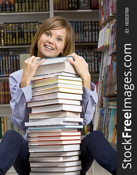 Young smilling woman sitting with stack of books in the library. Young smilling woman sitting with stack of books in the library