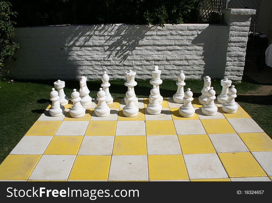 White chess pieces on a giant outdoor chess board.