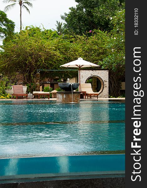 A tropical infinity pool with water bubble, water fountain and pool side bed on a tropical greenery background. Picture taken in a resort along Kuta beach in Bali, Indonesia.