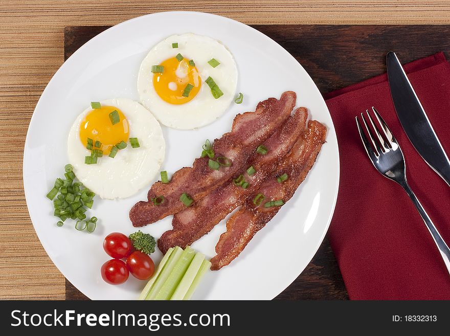 Fried eggs with fried bacon and vegetables.