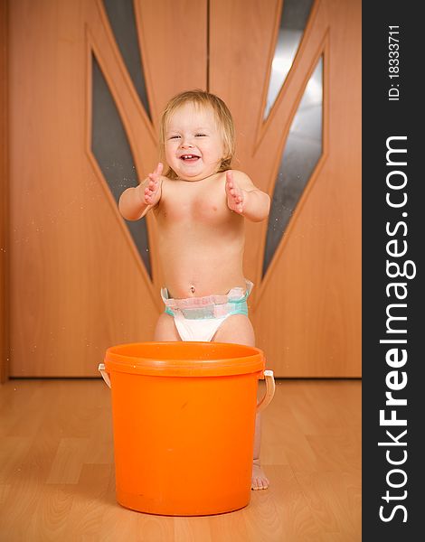 Adorable happy baby applause staying near orange pail washing floor