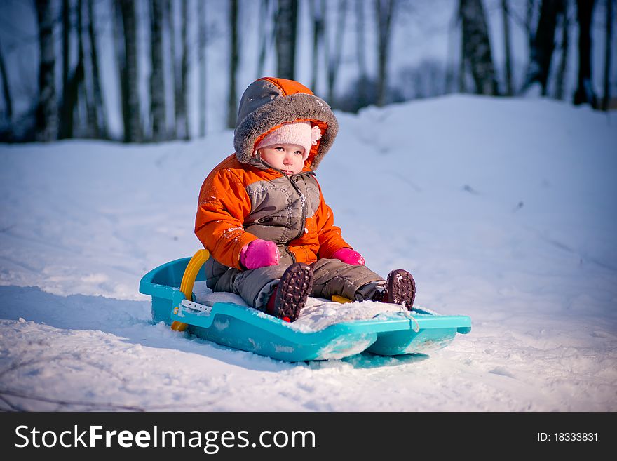 Serious baby sliding on sleigh from hill