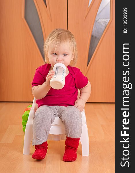 Adorable baby sit on baby chair toilet and drink milk from bottle. Adorable baby sit on baby chair toilet and drink milk from bottle