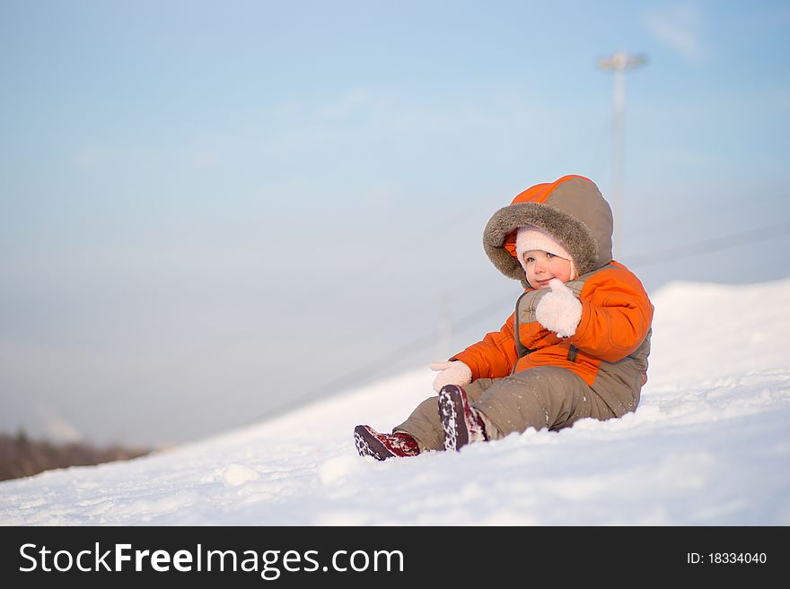 Adorable baby sit on mountain side on sunset and try to slide down