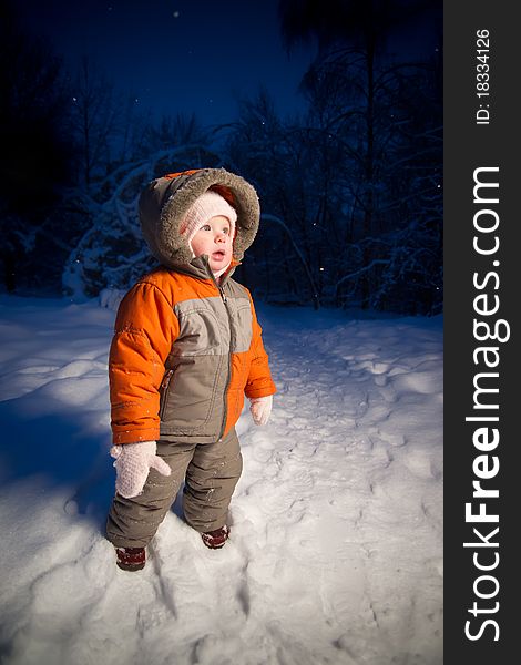 Adorable baby walking in evening park. Stay on snow road look side