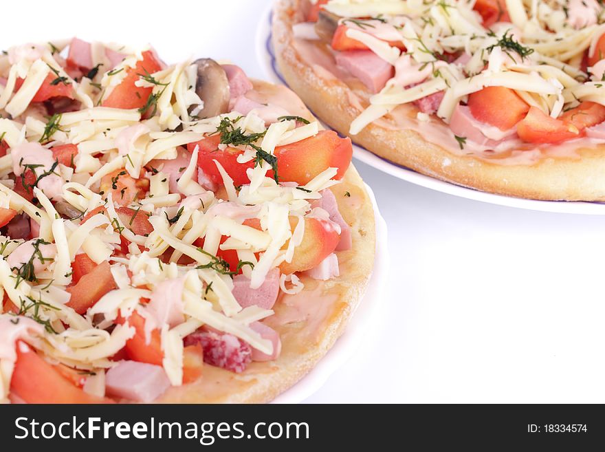 Two fresh pizzas with tomatoes, sauce, ham, sausage, cheese, dill ready for cooking isolated on white background