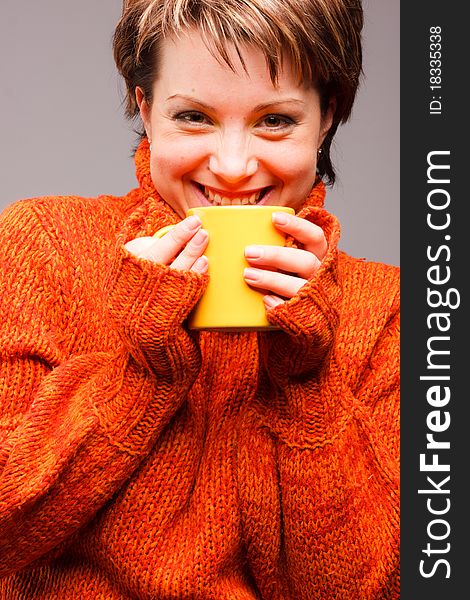 Charming  beautiful woman in the sweater of orange color with a mug in hands. Charming  beautiful woman in the sweater of orange color with a mug in hands