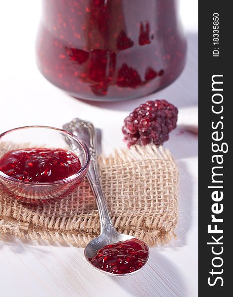 Raspberry jam in glass with silver spoon on white table