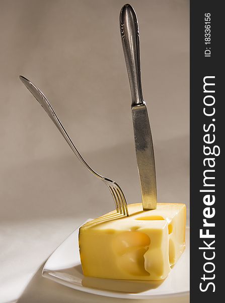 Knife and fork stick in cheese on grey background. Knife and fork stick in cheese on grey background