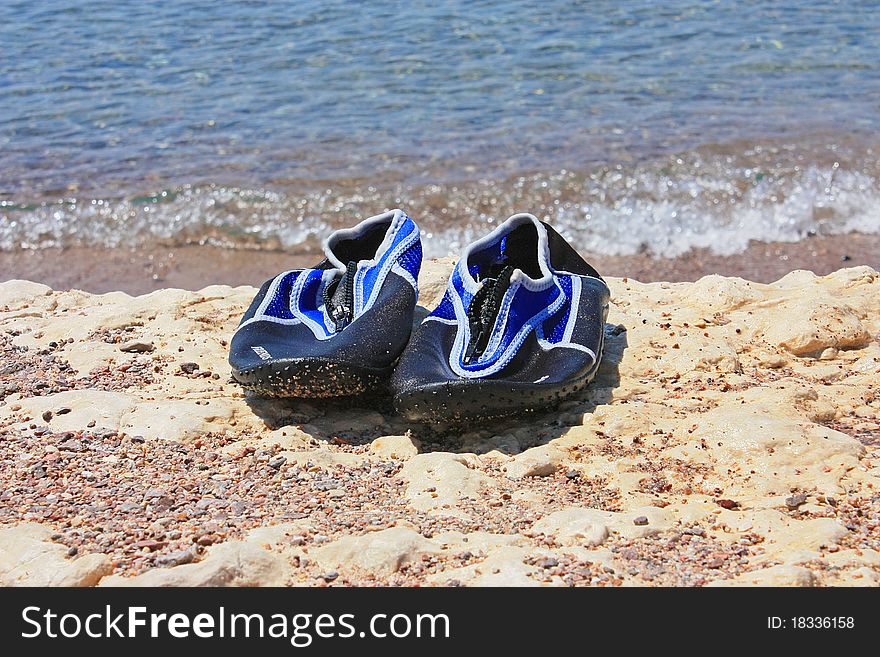 Swimming shoes on white stone with beautiful blue water in the background. Swimming shoes on white stone with beautiful blue water in the background.