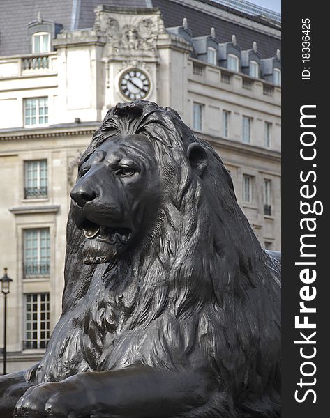 A lion statue sits under the clock of an ornate building Trafalgar Square, London. A lion statue sits under the clock of an ornate building Trafalgar Square, London.