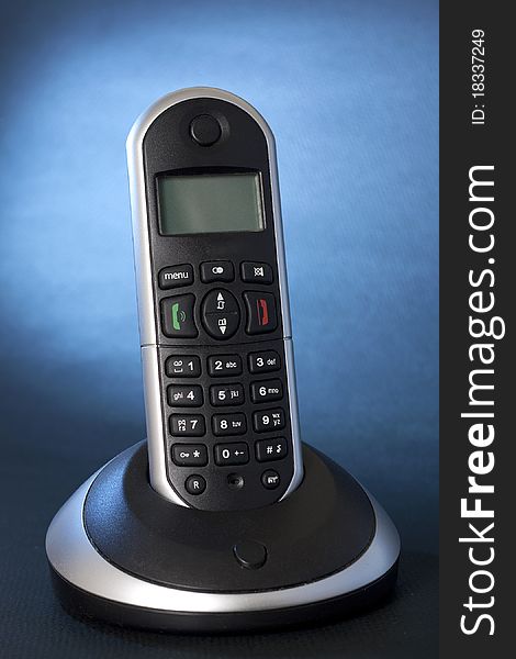 A black wireless telephone on a cradle, background focus with blue gel