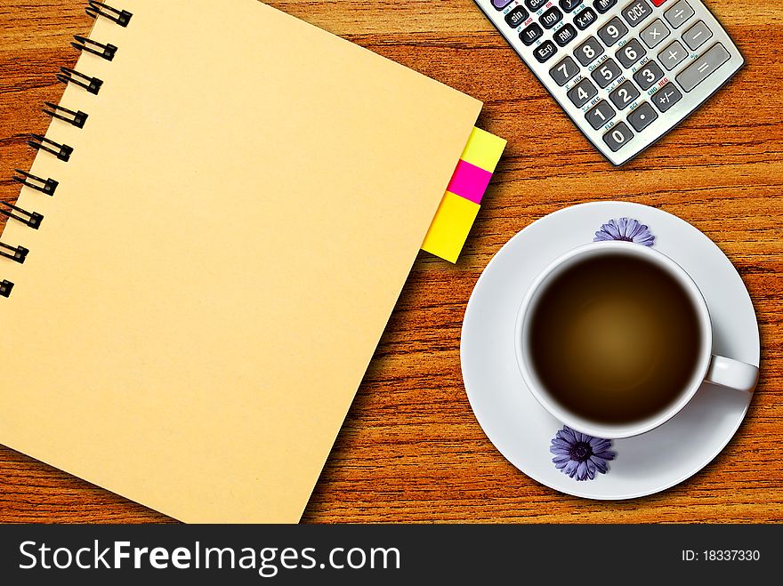 White cup of coffee and calculator on notebook on wood table background. White cup of coffee and calculator on notebook on wood table background