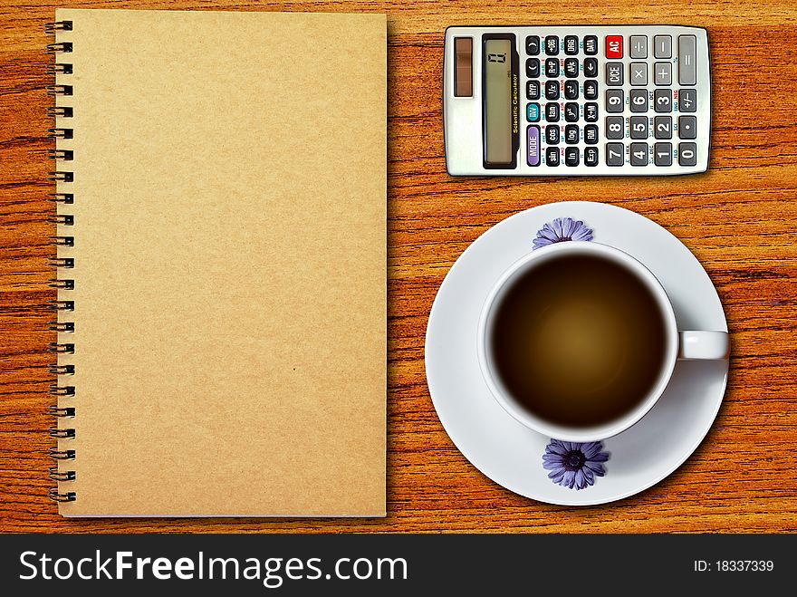 White cup of coffee and calculator on notebook on wood table background. White cup of coffee and calculator on notebook on wood table background