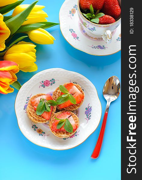 Cakes with fresh strawberry and mint and yellow tulips on blue background