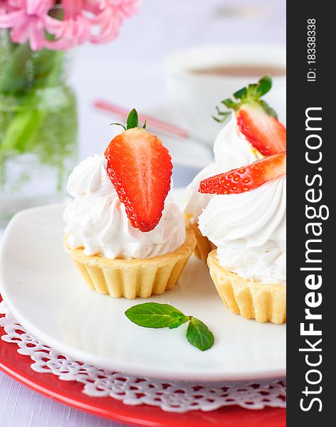 Cake with white protein cream and strawberry on white plate and soft background filled with white cup of tea and hyacinth flowers