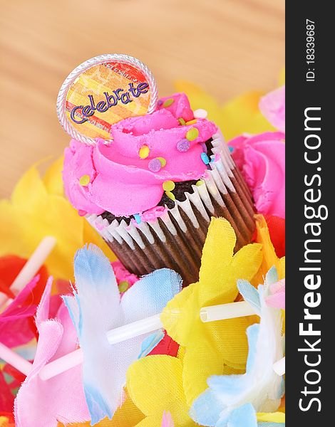 Cupcake with pink icing and celebrate medallion surrounded by a colorful lei. Cupcake with pink icing and celebrate medallion surrounded by a colorful lei