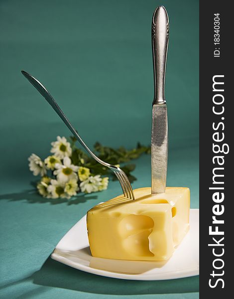 Knife and fork stick in cheese on cyan background. Knife and fork stick in cheese on cyan background