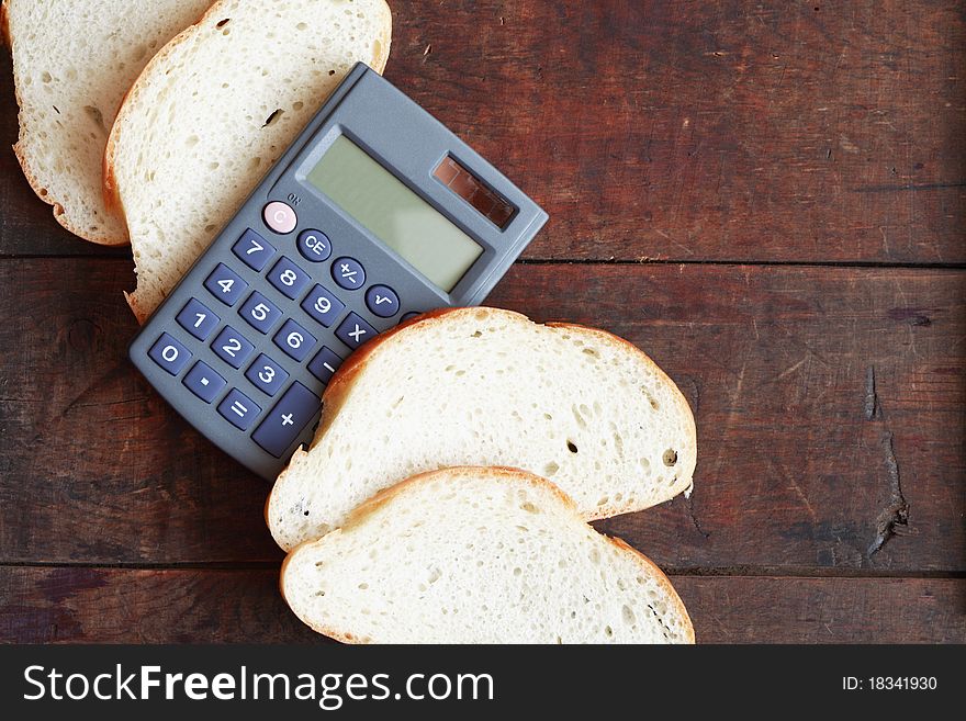 Sliced white bread and calculator lying on wooden surface with copy space. Sliced white bread and calculator lying on wooden surface with copy space