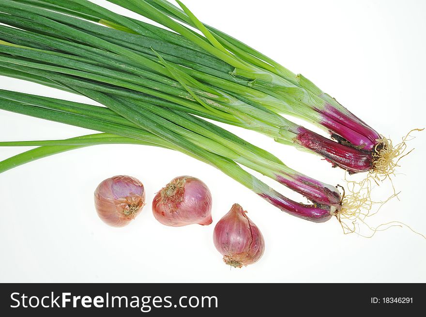 Green Leafy Spring Onions And Red Onions Arranged On A White Background