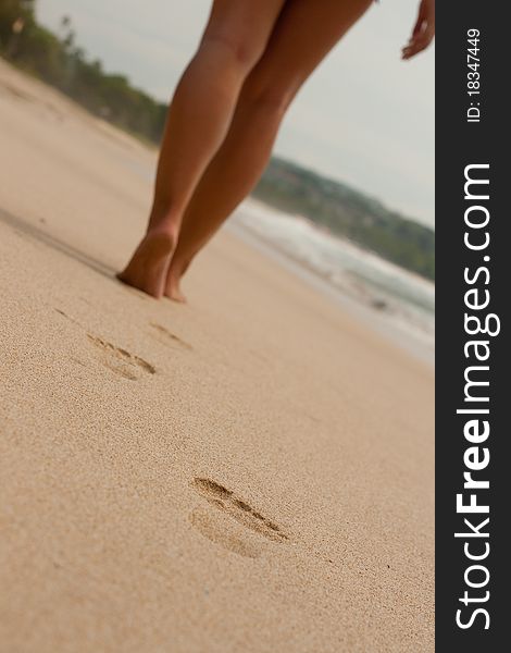 Image of women's legs on the beach and footprints in the sand