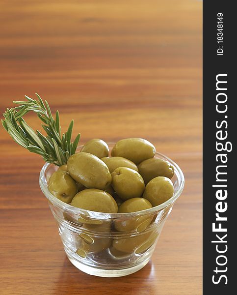 Jar of green olives and rosemary on wooden table background