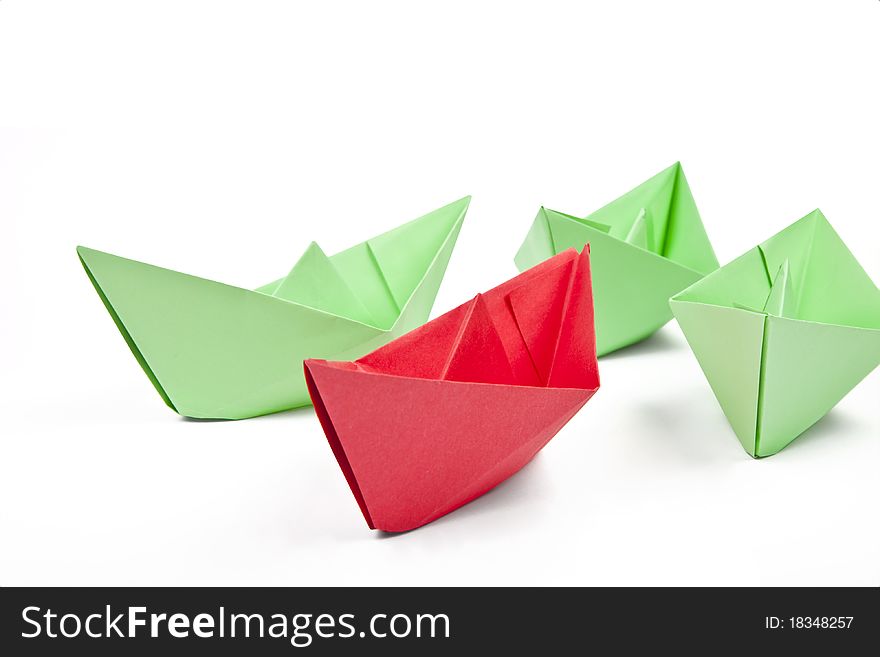 Single red paper boat between lots of green paper boats on white