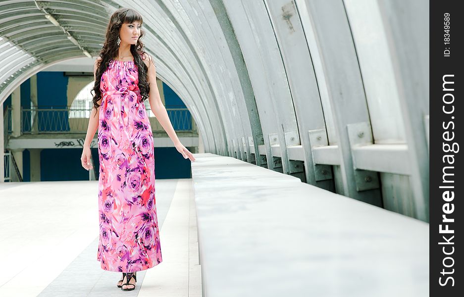 The beautiful girl in a long dress is by the window in a pedestrian crossing