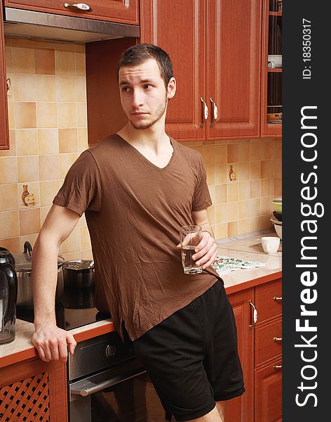 Guy in the kitchen with glass of water, wearing shorts and shirt