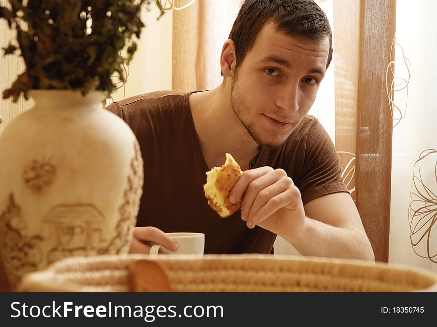 Young guy with tea and cake in the kitchen