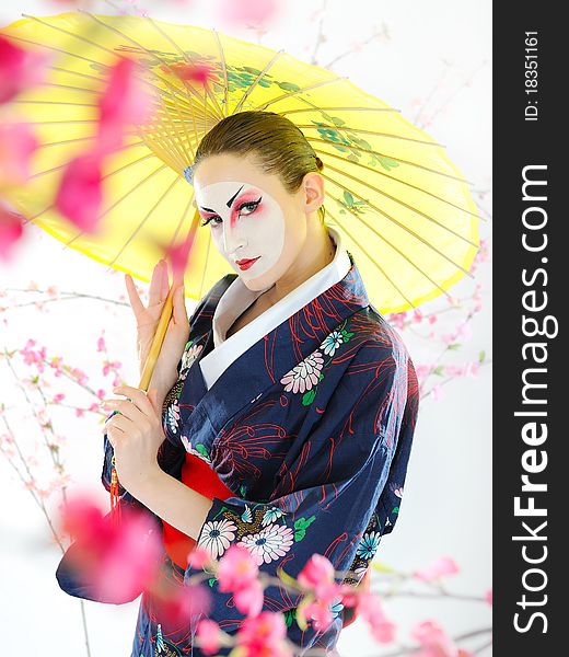 Artistic portrait of japan geisha woman with creative make-up near sakura tree in kimono with umbrella