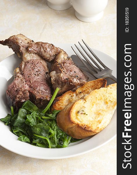 Delicious lamb chops with garlic bread and spinach on a plate