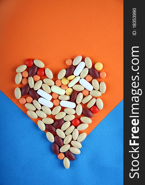 Pills in shape of love heart on orange and blue background. Pills in shape of love heart on orange and blue background