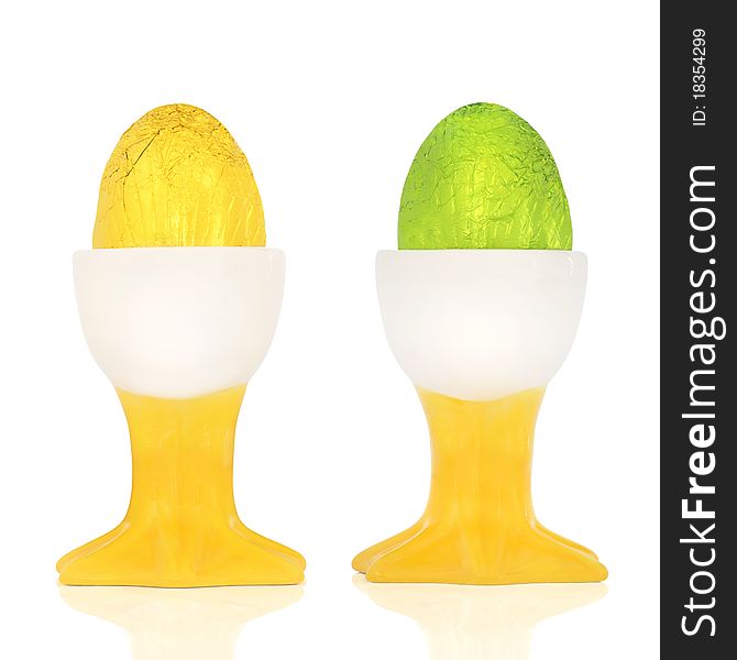 Chocolate easter eggs wrapped in coloured foil, in egg cups, over white background. Chocolate easter eggs wrapped in coloured foil, in egg cups, over white background.