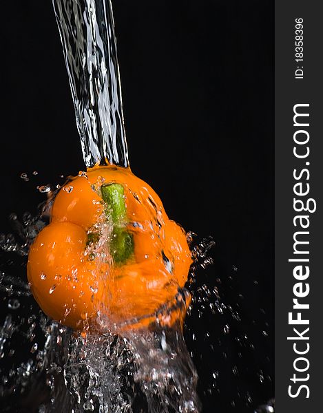 Orange bell pepper in water stream on black background. Orange bell pepper in water stream on black background