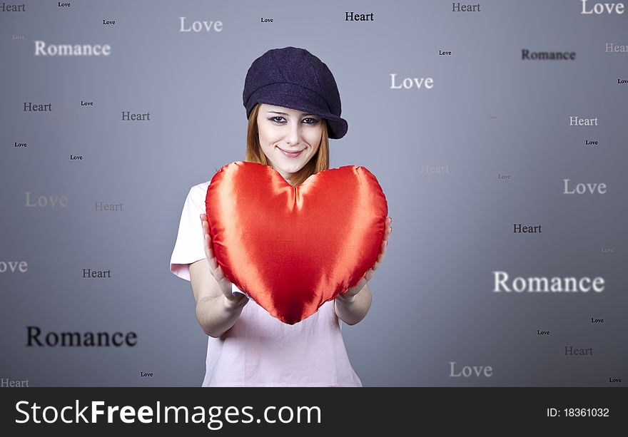 Beautiful red-haired girl in cap with toy heart. Studio shot.