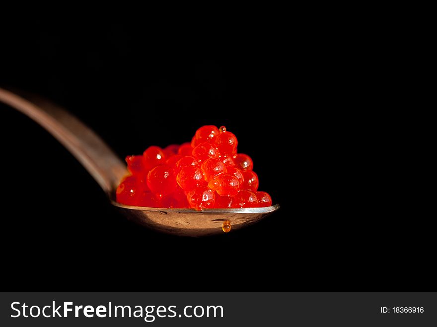 Spoon with red caviar isolated on black background