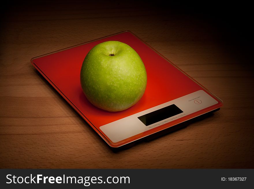 Apple is in the scales, standing on a wooden surface.