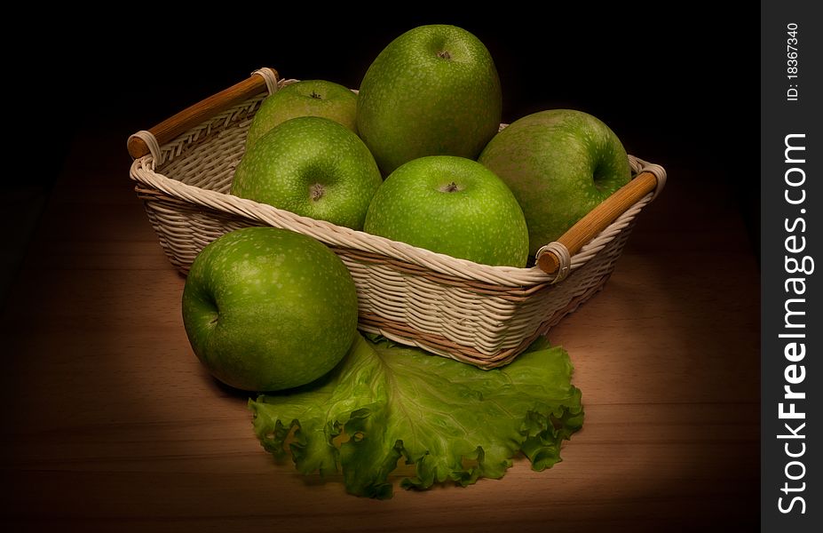 Apples in a wicker basket, standing on a wooden surface.