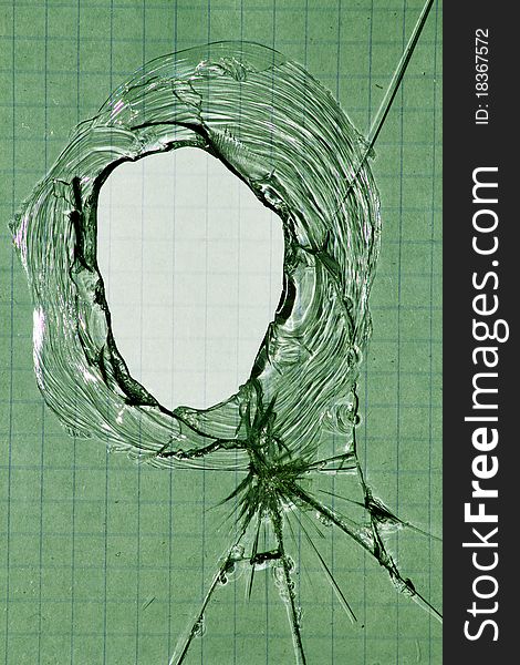 Hole and cracks in glass against a sheet of paper with cages. Hole and cracks in glass against a sheet of paper with cages