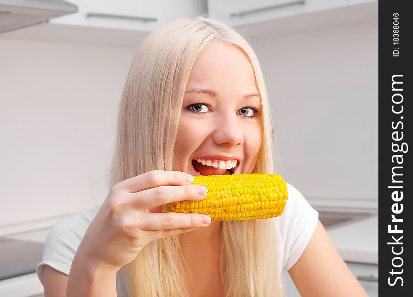 Beautiful young blond woman eating corn in the kitchen at home. Beautiful young blond woman eating corn in the kitchen at home
