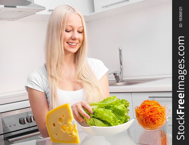 Beautiful young blond woman with salad, cheese and carrot in the kitchen at home. Beautiful young blond woman with salad, cheese and carrot in the kitchen at home