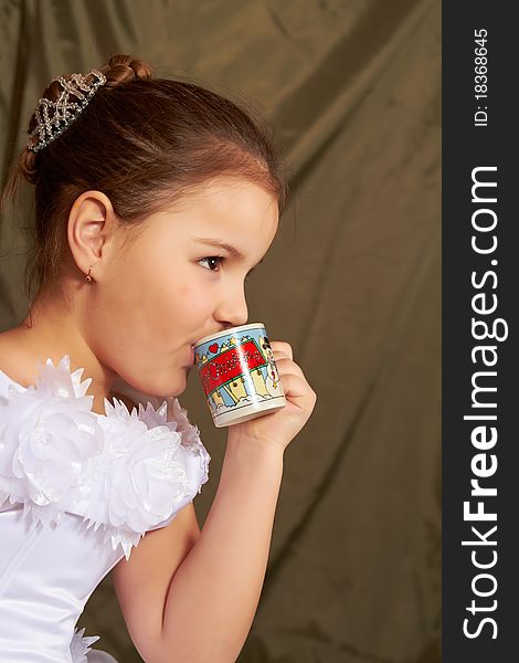 The little girl in a white dress drinks from a small cup. The little girl in a white dress drinks from a small cup.