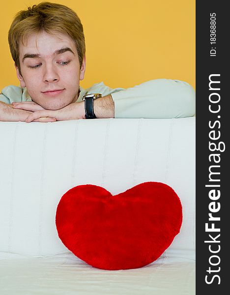 Blond young man looking at a red heart shaped pillow. Blond young man looking at a red heart shaped pillow