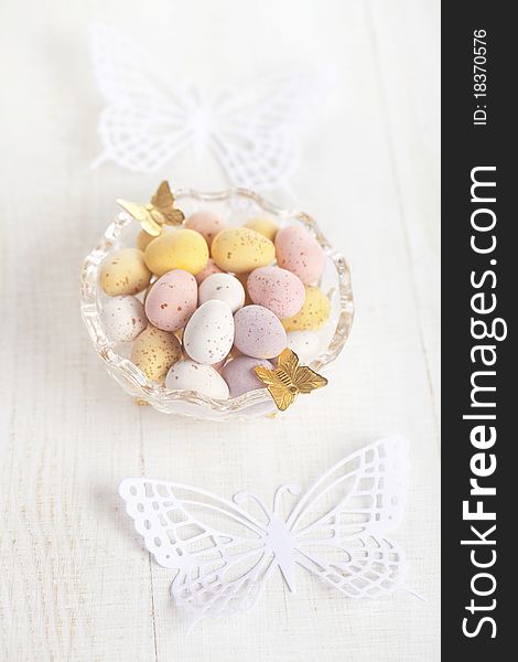 Easter chocolate speckled eggs in bowl with paper butterfly on white table, shallow dof